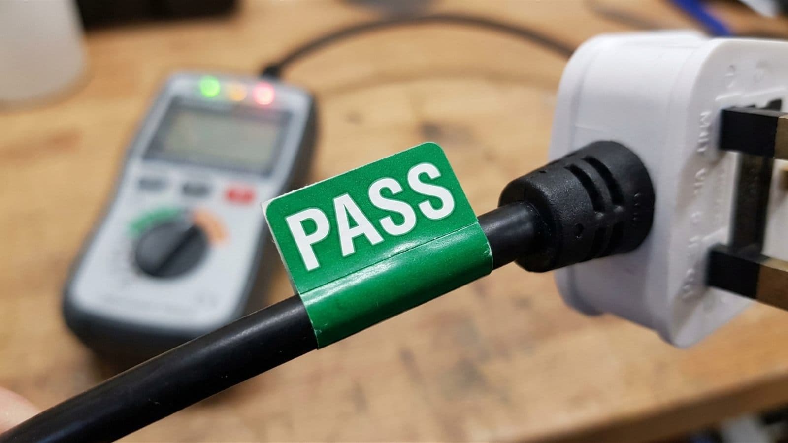 Green PASS label on the lead of a UK BS 1363 plug after a portable appliance test